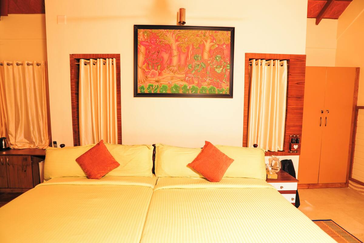 A hotel room with a bed, curtains, a painting, and a wardrobe.