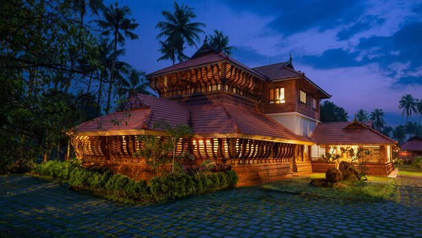 A traditional multi-story building with a tiled roof, surrounded by lush greenery and palm trees. - Neelambari Ecotourism Thrissur Aratupuzh (Thrissur)
