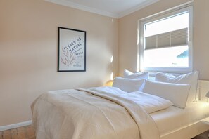 Un dormitorio con cama, almohadas, una ventana con persianas y una obra de arte enmarcada en la pared.