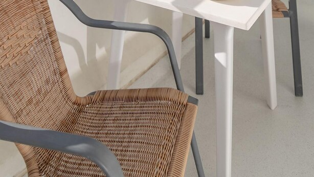 A balcony with wicker chairs, a table set with plates, glasses, and a fruit bowl.