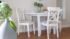 A dining area with a white table and chairs, a vase with flowers, and a decorative wall piece.