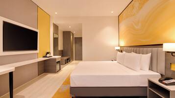 Habitación de hotel moderna con una cama grande, un televisor de pantalla plana, un escritorio y un baño visible a través de una puerta abierta.