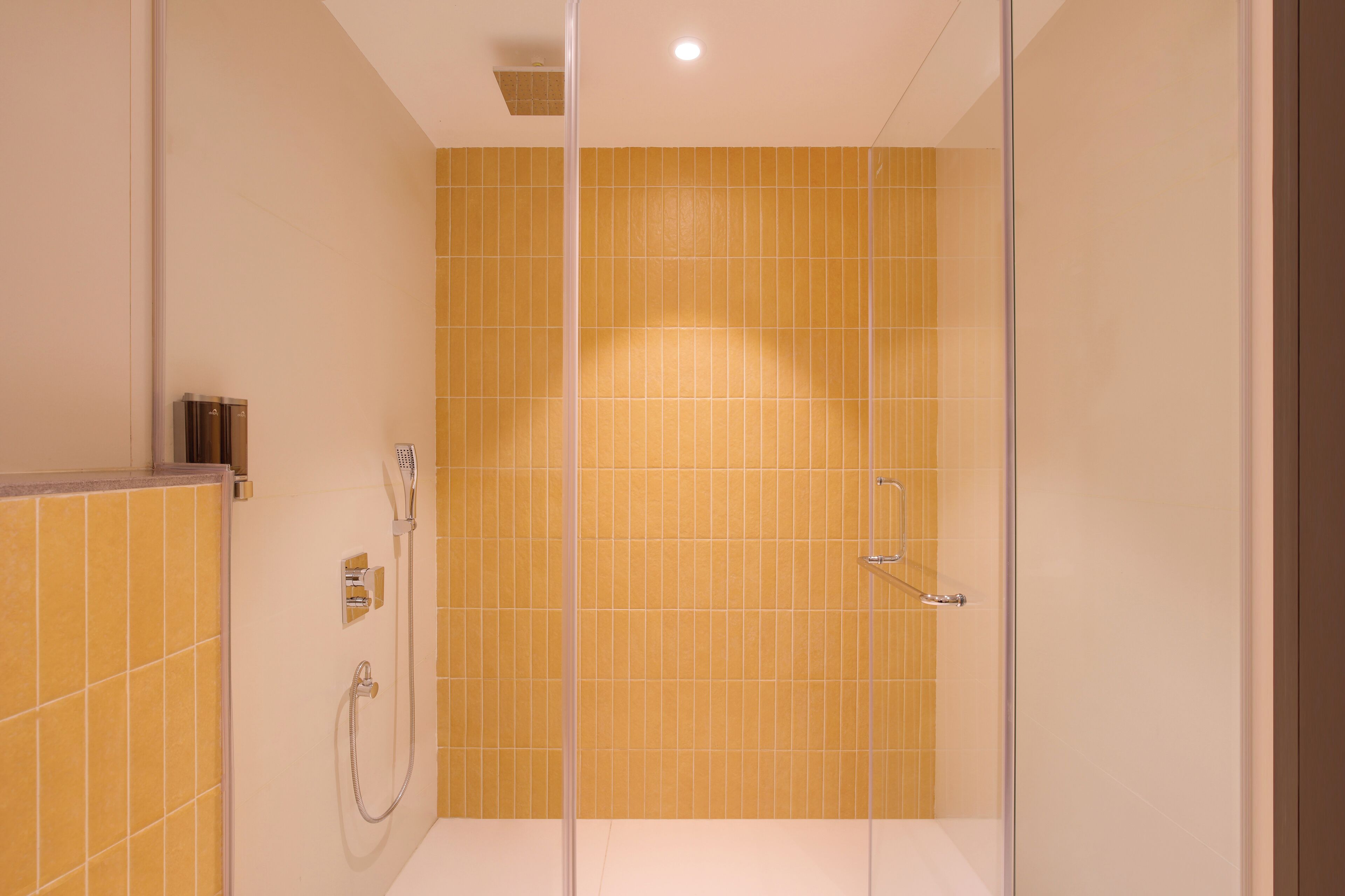 Une salle de bain moderne avec des carreaux jaunes, une douche en verre et un panneau de commande visible.