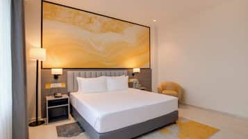 Een moderne hotelkamer met een groot bed, bedlampen, een nachtkastje, een stoel en een groot abstract schilderij aan de muur.