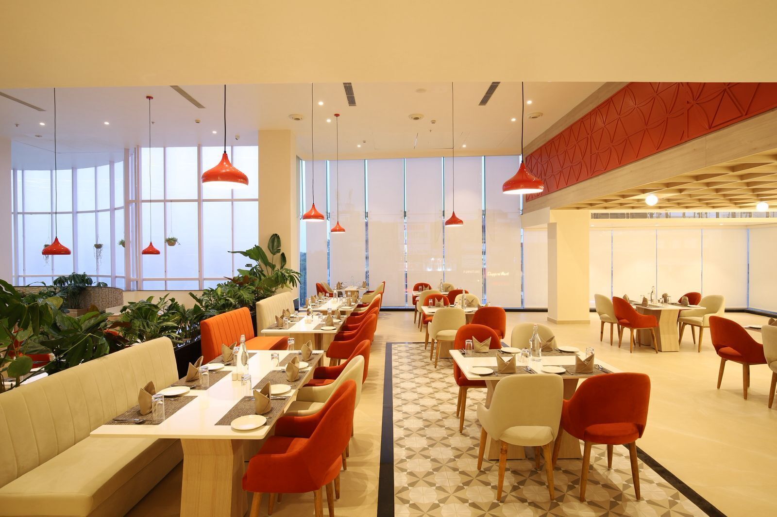 A modern dining area with long tables, orange chairs, and red pendant lights.