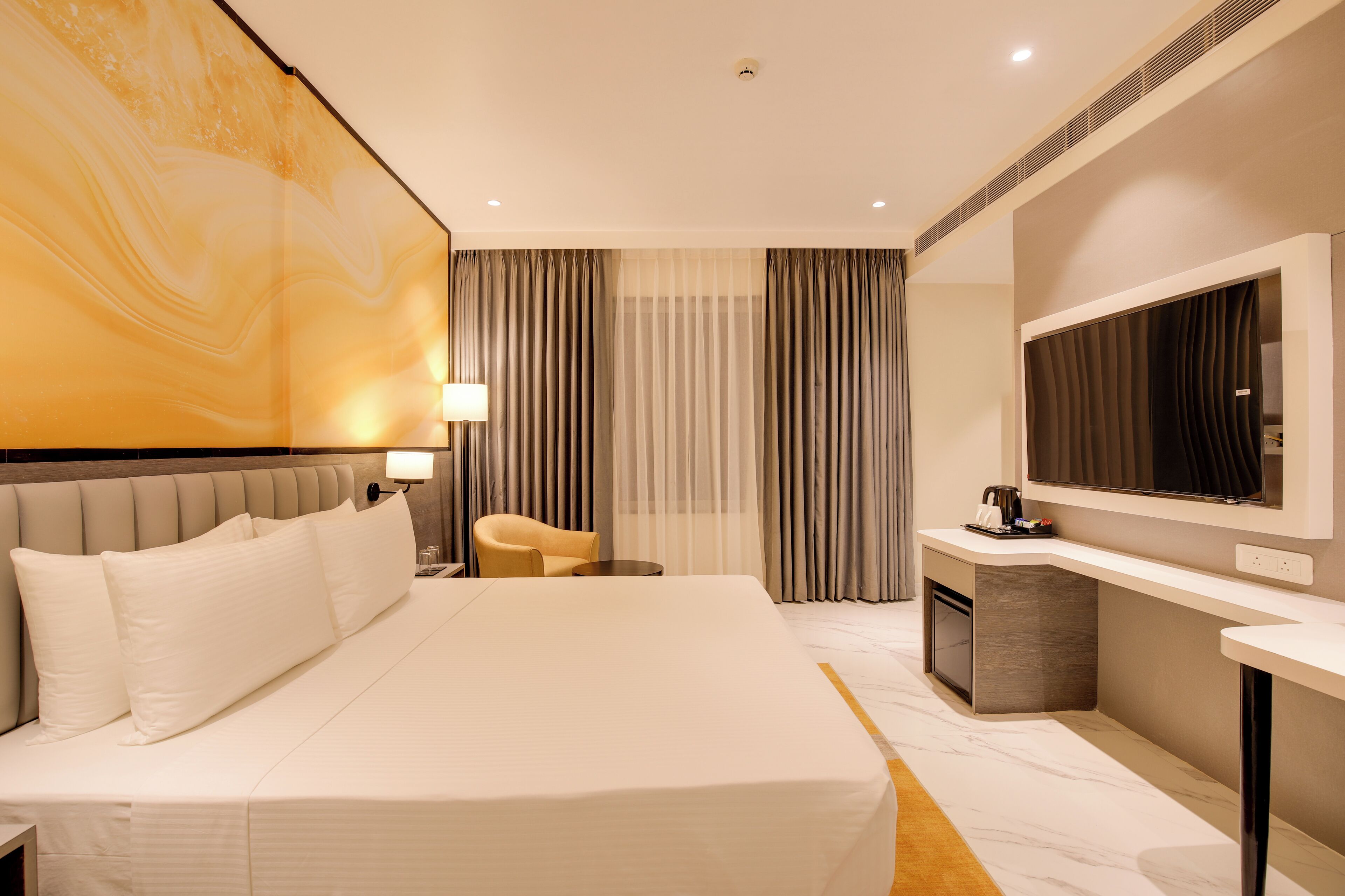A hotel room with a large bed, a desk, a chair, a TV, and curtains.