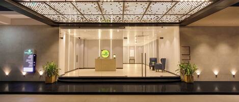 A modern reception area with a glass partition, a reception desk, and potted plants.