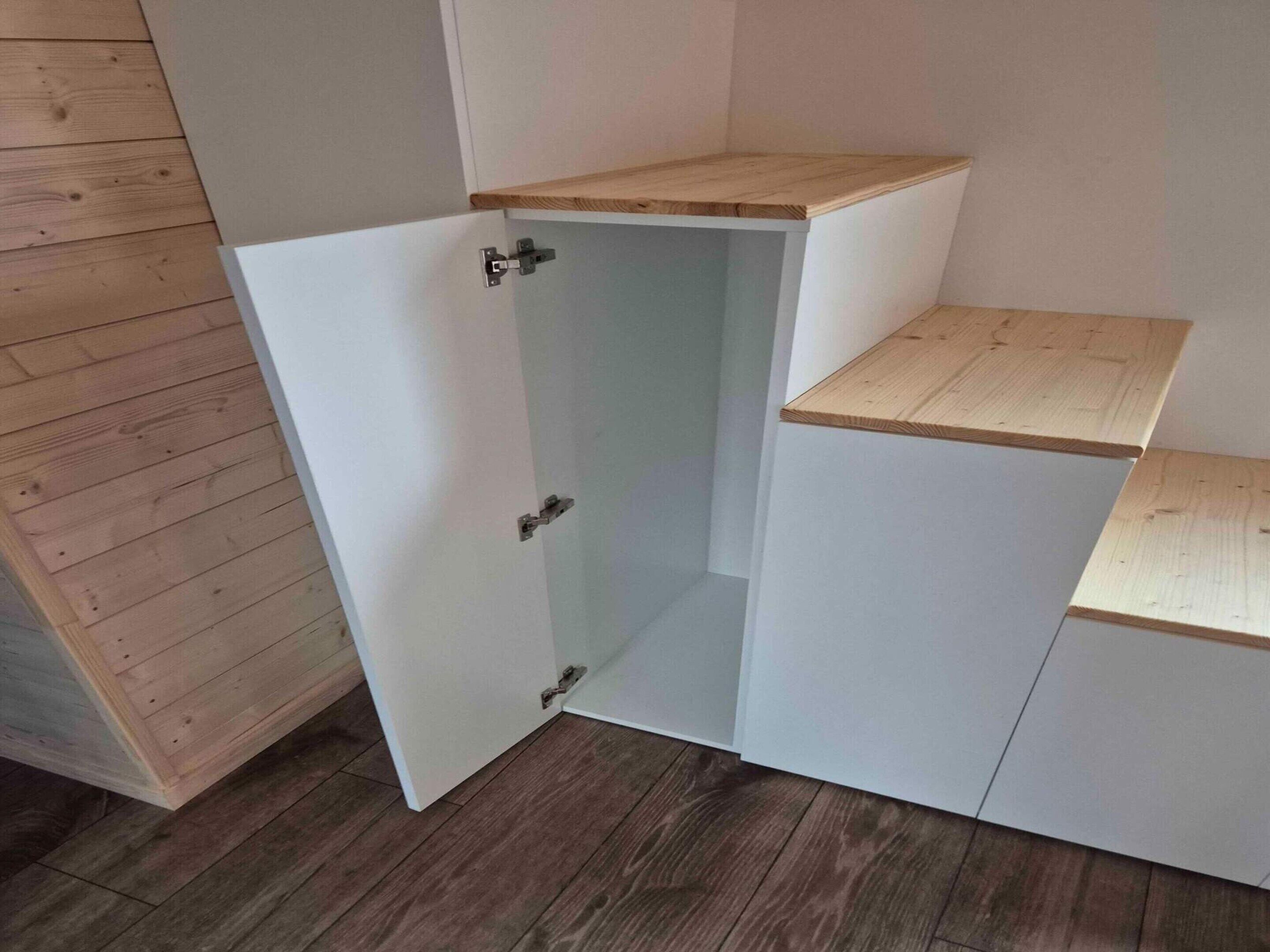 A corner cabinet with a wooden top shelf, a white door, and a small wooden countertop.
