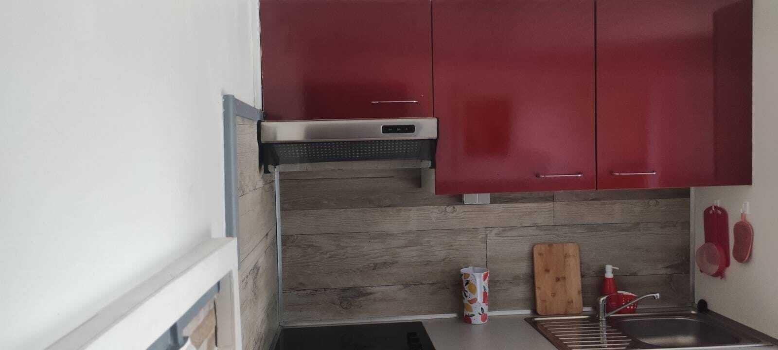 Une cuisine compacte avec des meubles rouges, une hotte en acier inoxydable, un pare-feu en bois, un évier et une planche à découper.