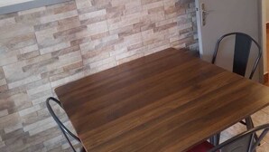 A dining area with a wooden table, metal chairs, a tiled wall with a stone accent, and a framed picture of a bird on the wall.