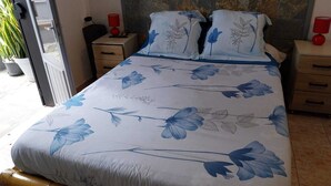 A bedroom with a bed featuring a floral bedspread, a stone headboard, bedside tables with lamps, and a sliding glass door leading to an outdoor area.