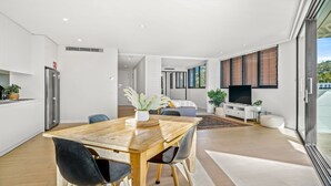 A modern kitchen with a built-in refrigerator, a dining area with a wooden table and chairs, and a living area with a TV and seating. - ROCKPOOL #101 | Walk to beach, WIFI | Accom Holidays (TERRIGAL)