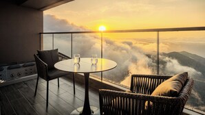 A balcony with a round table and two chairs, overlooking a mountainous landscape with clouds and a setting sun. - NaiBnB in Antara Genting (Genting Highlands)