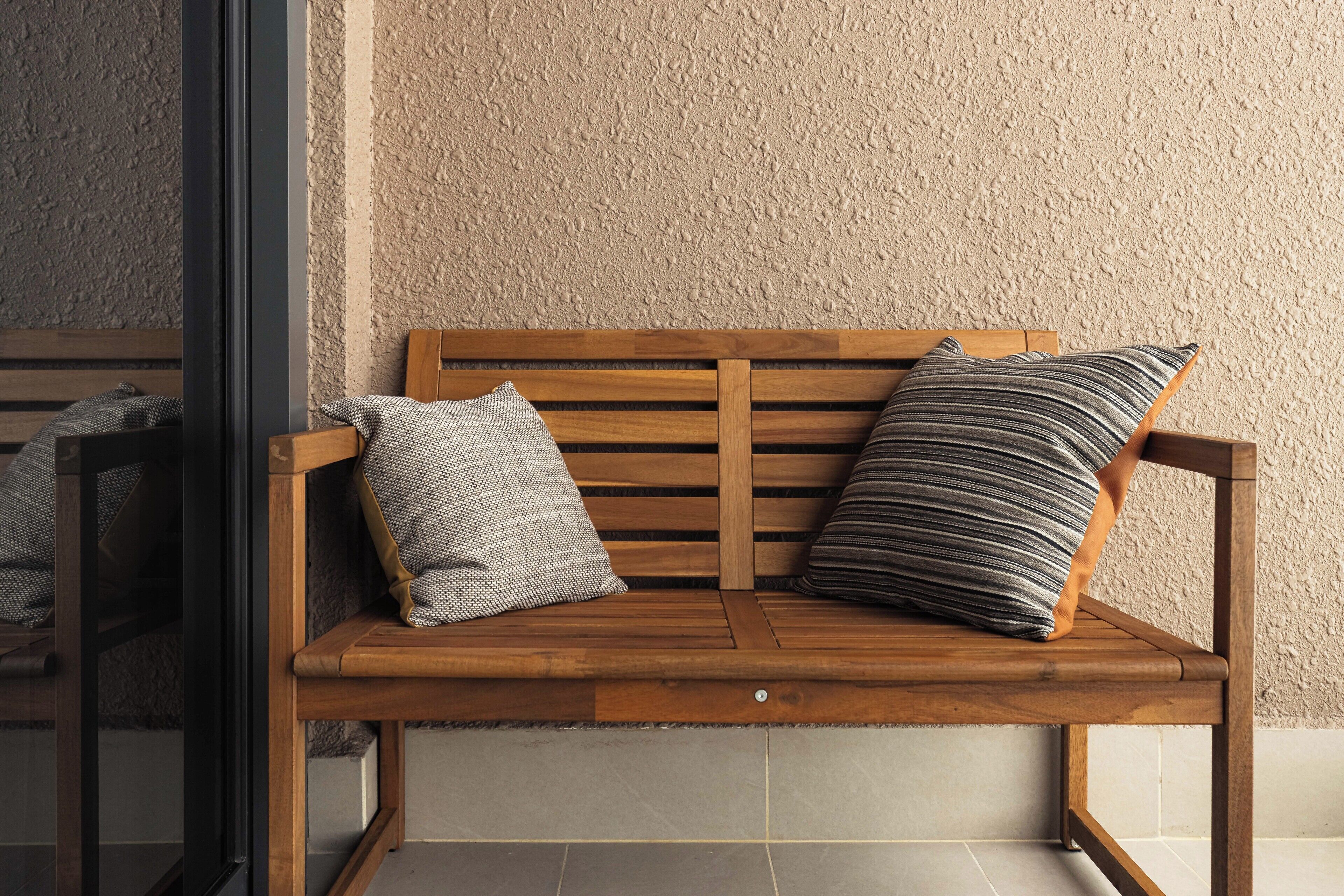 Un banc en bois avec deux coussins, adossé à un mur à texture.