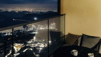 Ein Balkon mit Blick auf die Stadt, ein Tisch mit zwei weißen Tassen und ein schwarzer Sitzhocker.