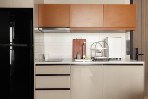 Una cocina moderna con un refrigerador negro, armarios de madera, una campana extractora de acero inoxidable y un salpicadero de azulejos blancos.