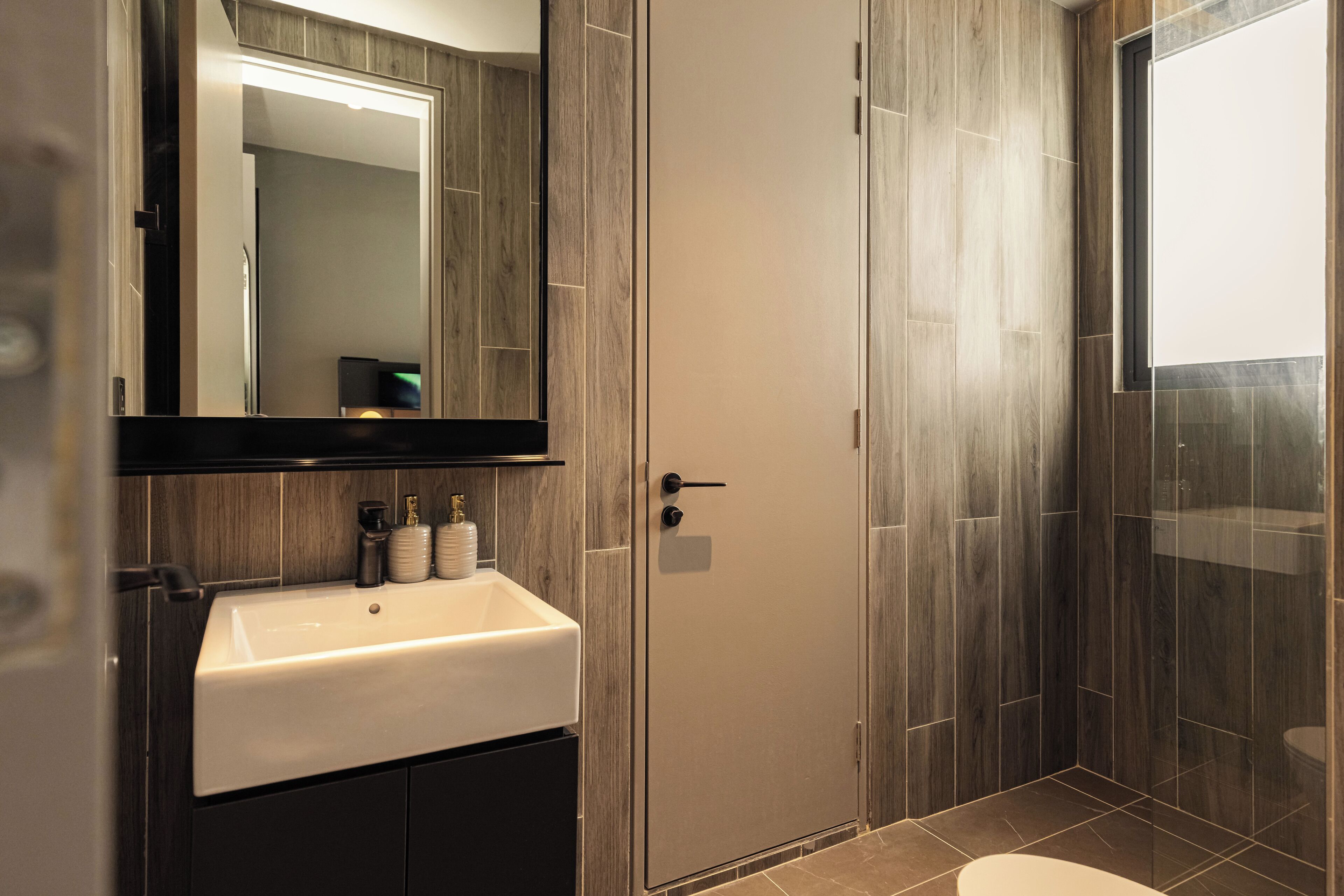 Une salle de bain moderne avec un lavabo blanc, un lambris en bois foncé et une cabine de douche en verre.