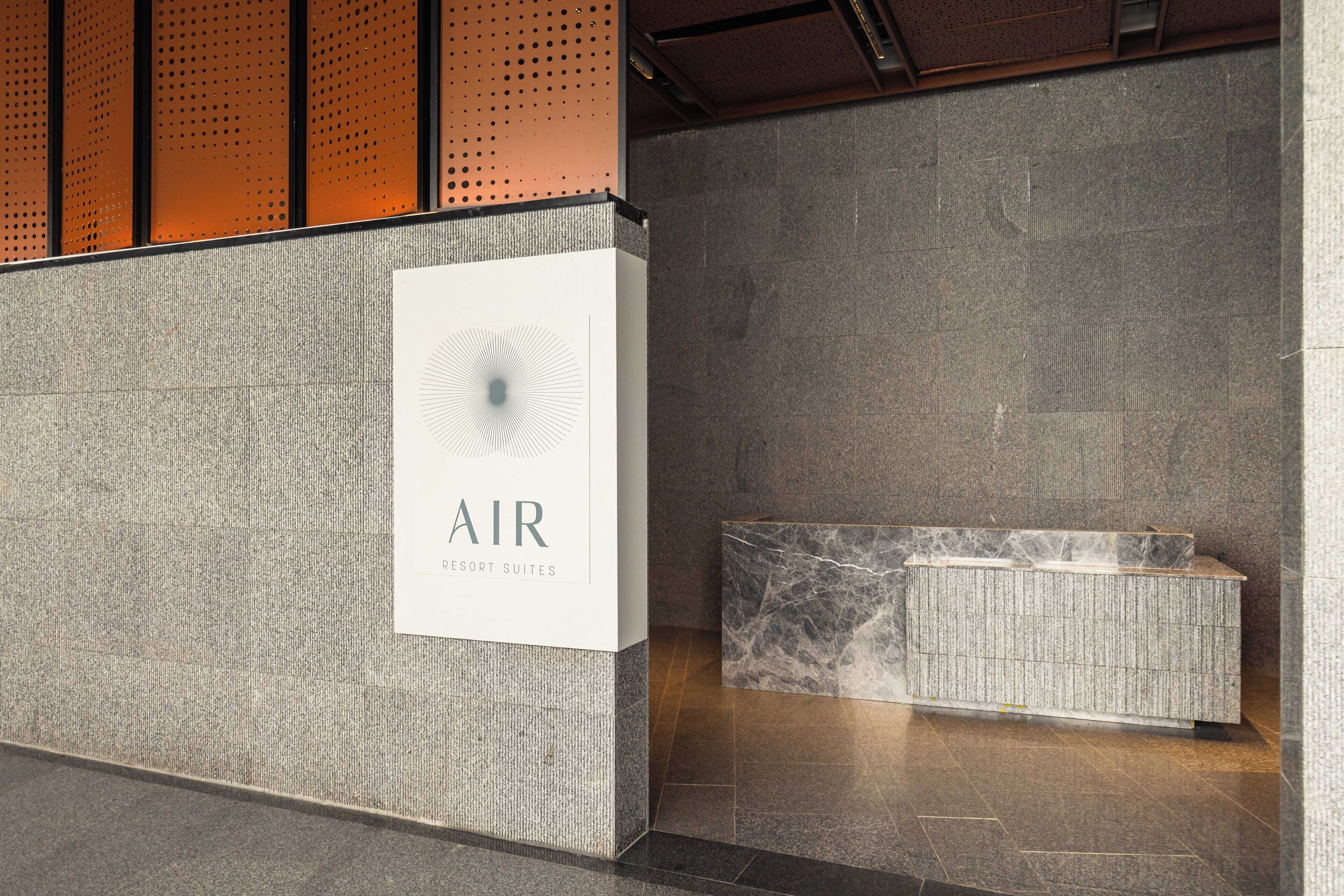 A reception area with a sign reading "AIR Resort Suites," a marble bench, and a textured wall.