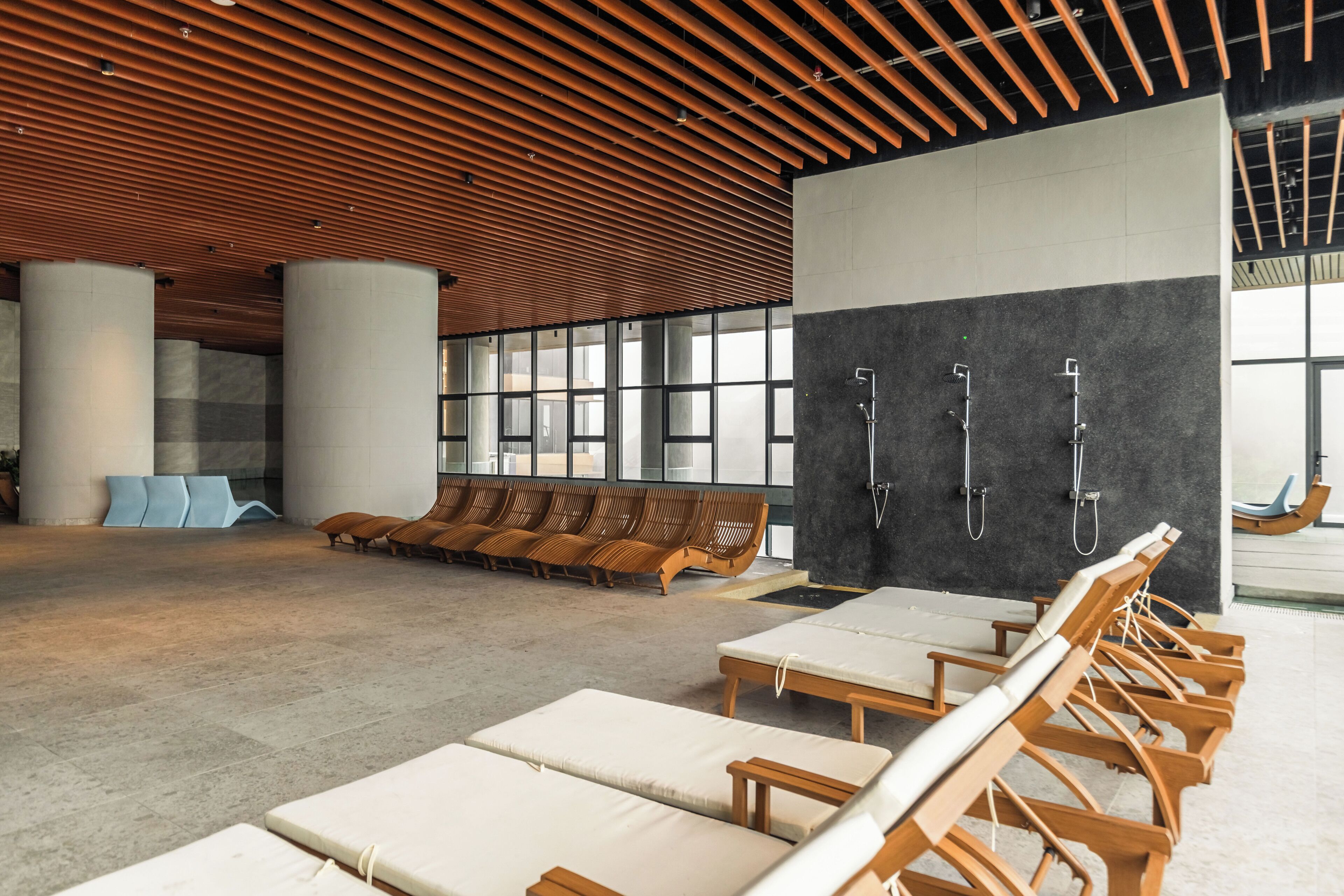 Un espacio interior amplio con techos de listones de madera, ventanas grandes y mobiliario que incluye sillones y bancos.