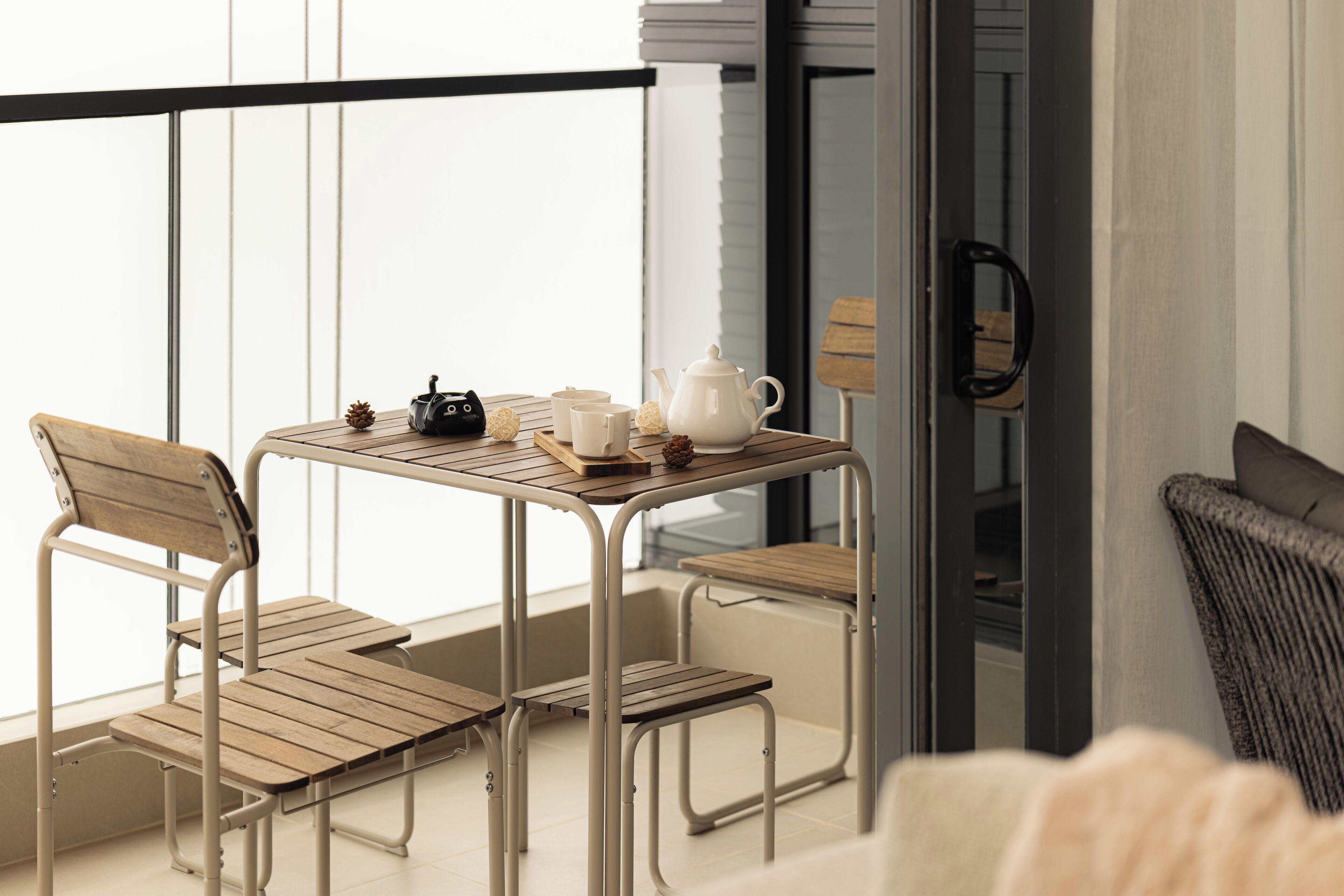 A balcony with a table set for tea, featuring a teapot, cups, and a small decorative item.