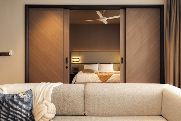 Une chambre d’hôtel avec un canapé, un lit avec une tête de lit, un ventilateur de plafond et une porte coulissante.