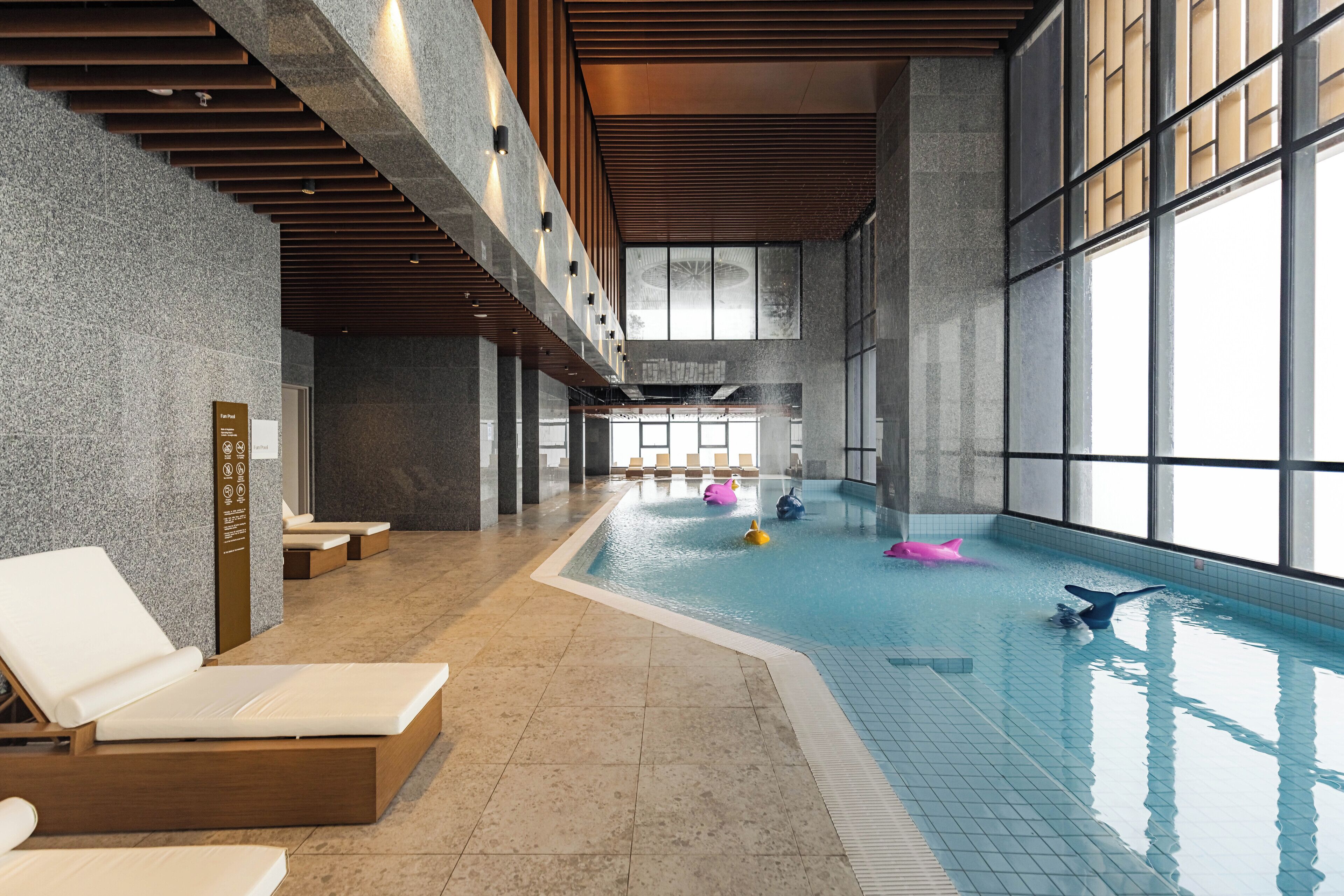 An indoor swimming pool with lounge chairs and a large window.