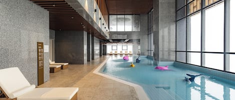 An indoor swimming pool with lounge chairs and a large window.