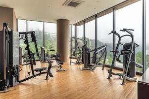 Un gimnasio con diversas máquinas de ejercicio, amplias ventanas y vistas a zonas verdes.
