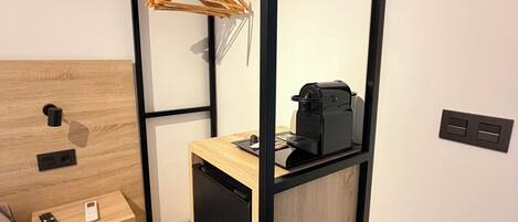 Una habitación compacta con una cama, un pequeño escritorio, un electrodoméstico negro y un armario de madera.