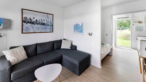 A modern living room with a grey sectional sofa, a small white table, and a cityscape painting. - 5 Star Holiday Home in Nexo (Nexø)