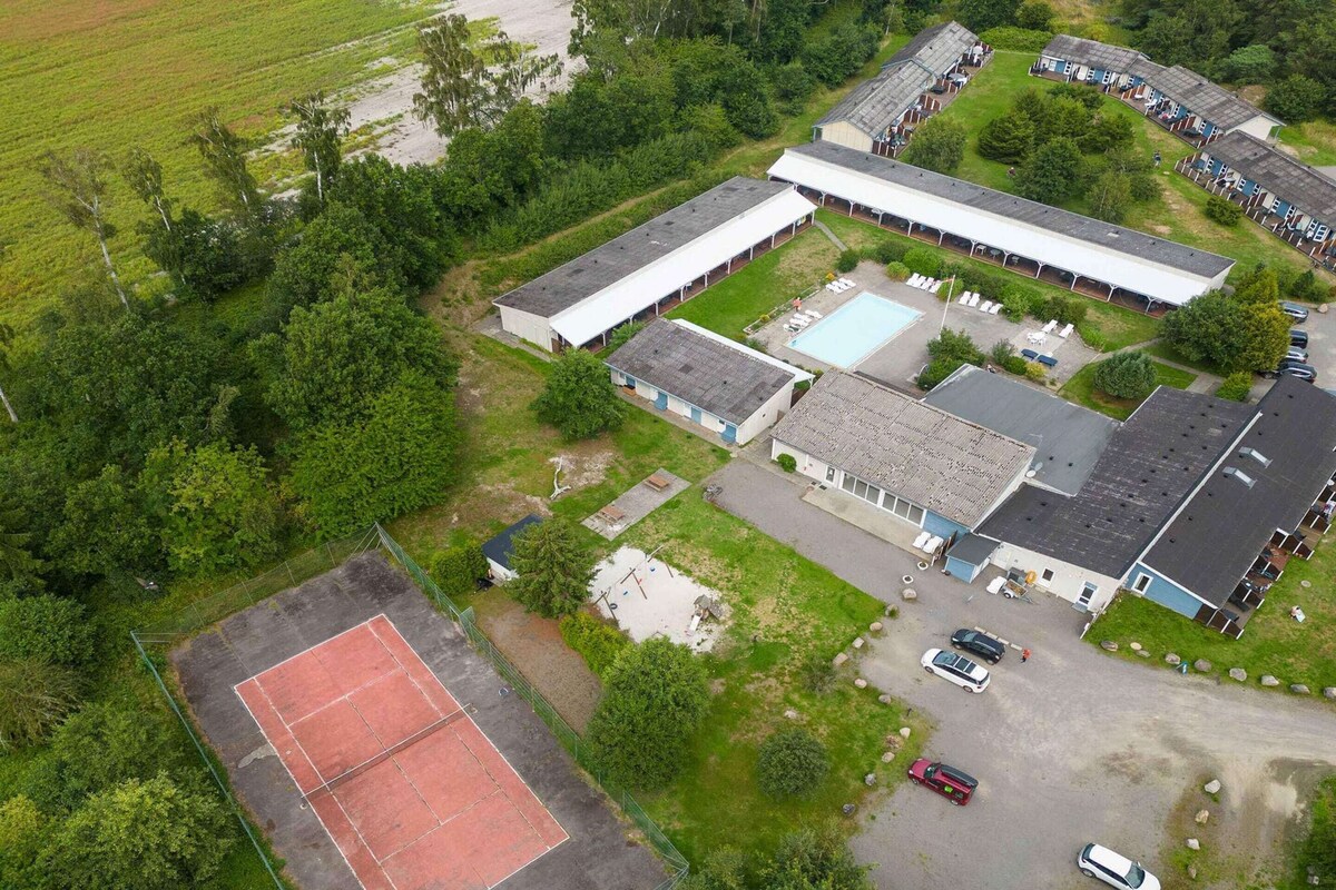 An aerial view of a property with a large building, a tennis court, and several cars parked.