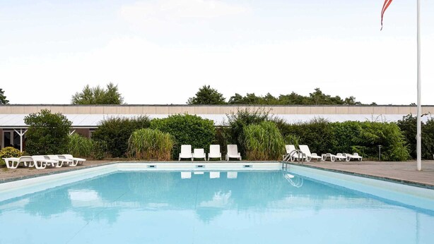 A swimming pool with white lounge chairs and a flagpole. - 5 Star Holiday Home in Nexo (Nexø)