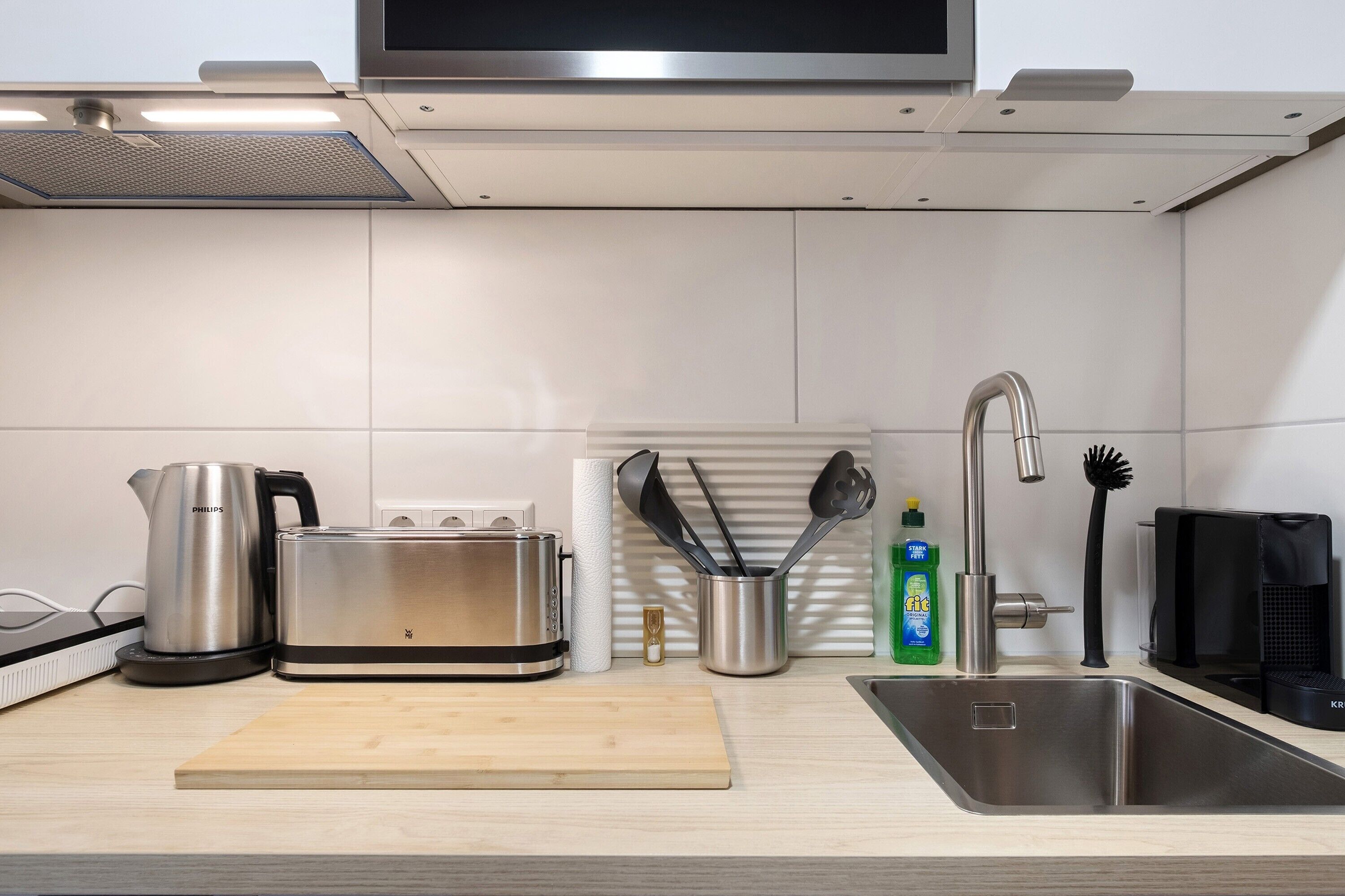 A modern kitchen with a toaster, kettle, sink, and various utensils.