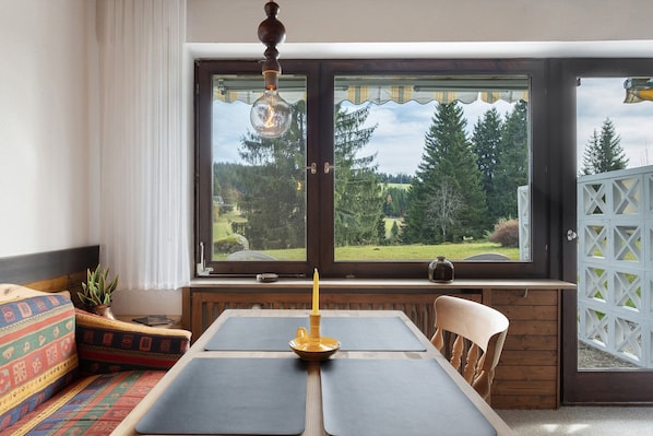 Una habitación con un ventanal grande, una mesa con una vela, una silla y un banco con cojines.