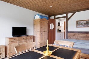 Una habitación con techo de madera, un televisor sobre un mueble de madera, una cama con colchón azul y un cuadro en la pared.