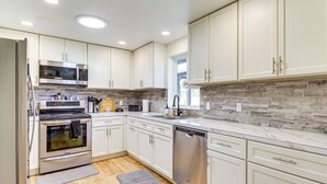 A modern kitchen with white cabinets, stainless steel appliances, a marble backsplash, and wooden flooring. - Water Views & Hot Tub: 'Kim's Kastle' in Stanwood! (Stanwood)