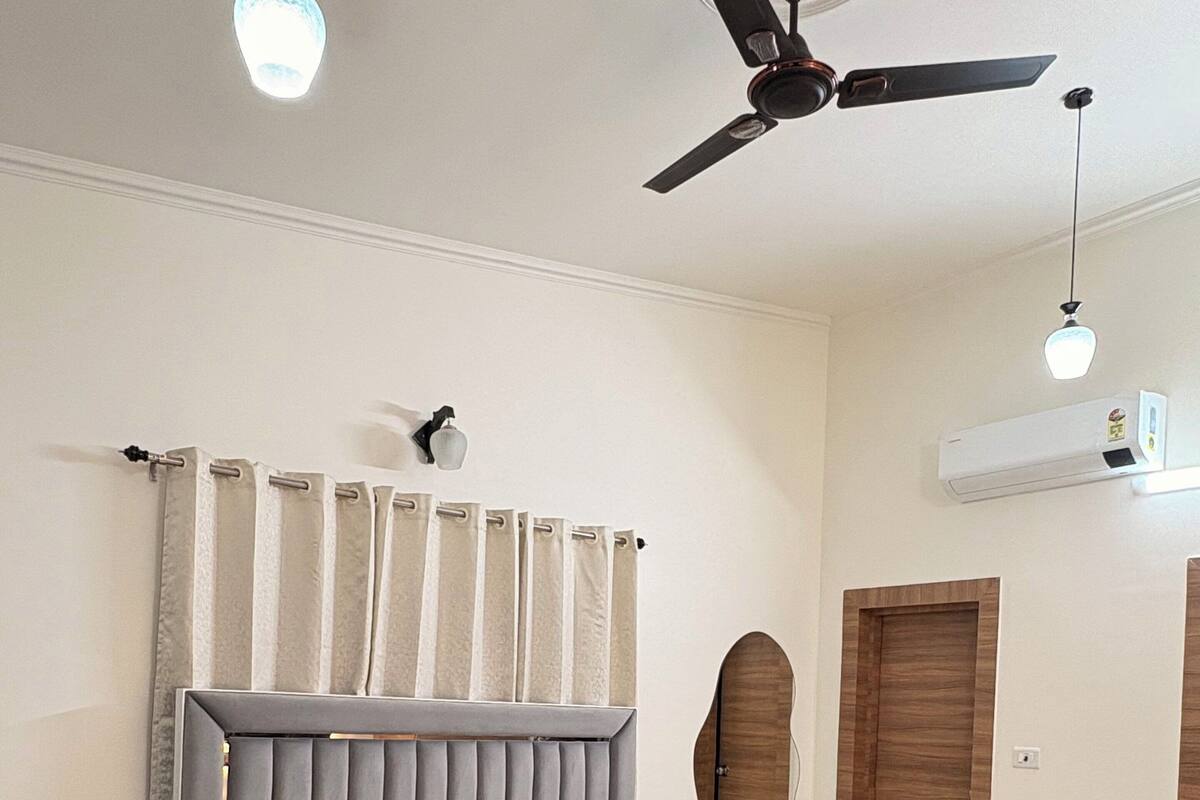 A bedroom with a bed, a ceiling fan, an air conditioning unit, and a wooden wardrobe.