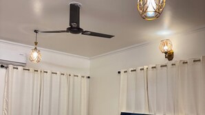 A bedroom with a bed, two chairs, a ceiling fan, and two pendant lights. - Noble Nook Stay - Bhimtal (Dungsilrawat)