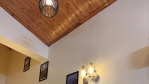 A staircase with wooden railings and a wooden ceiling. There are wall-mounted light fixtures and framed pictures on the wall. - Noble Nook Stay - Bhimtal (Dungsilrawat)