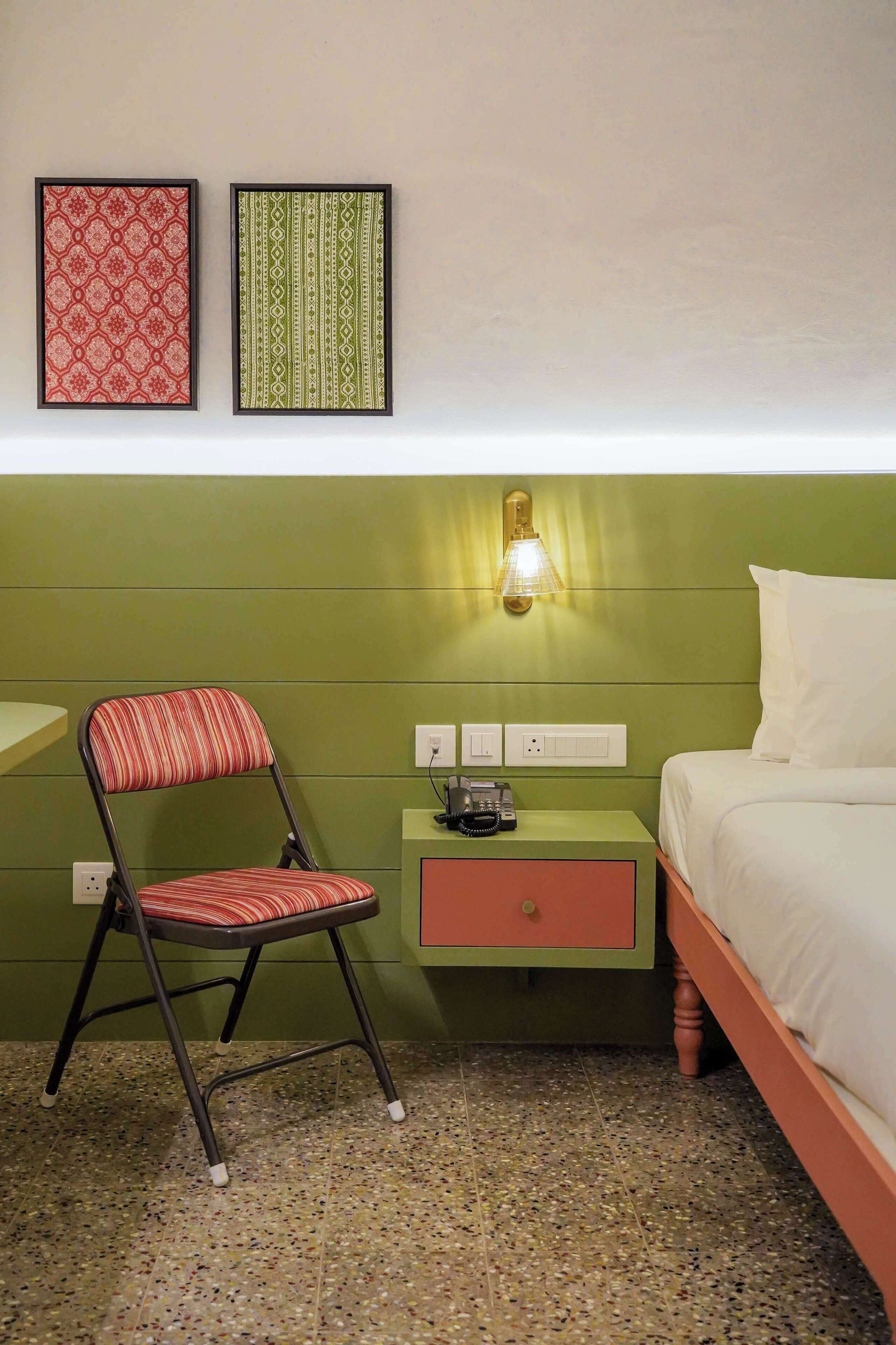 A room with a bed, a nightstand with a lamp, a chair, and two framed pictures on the wall.