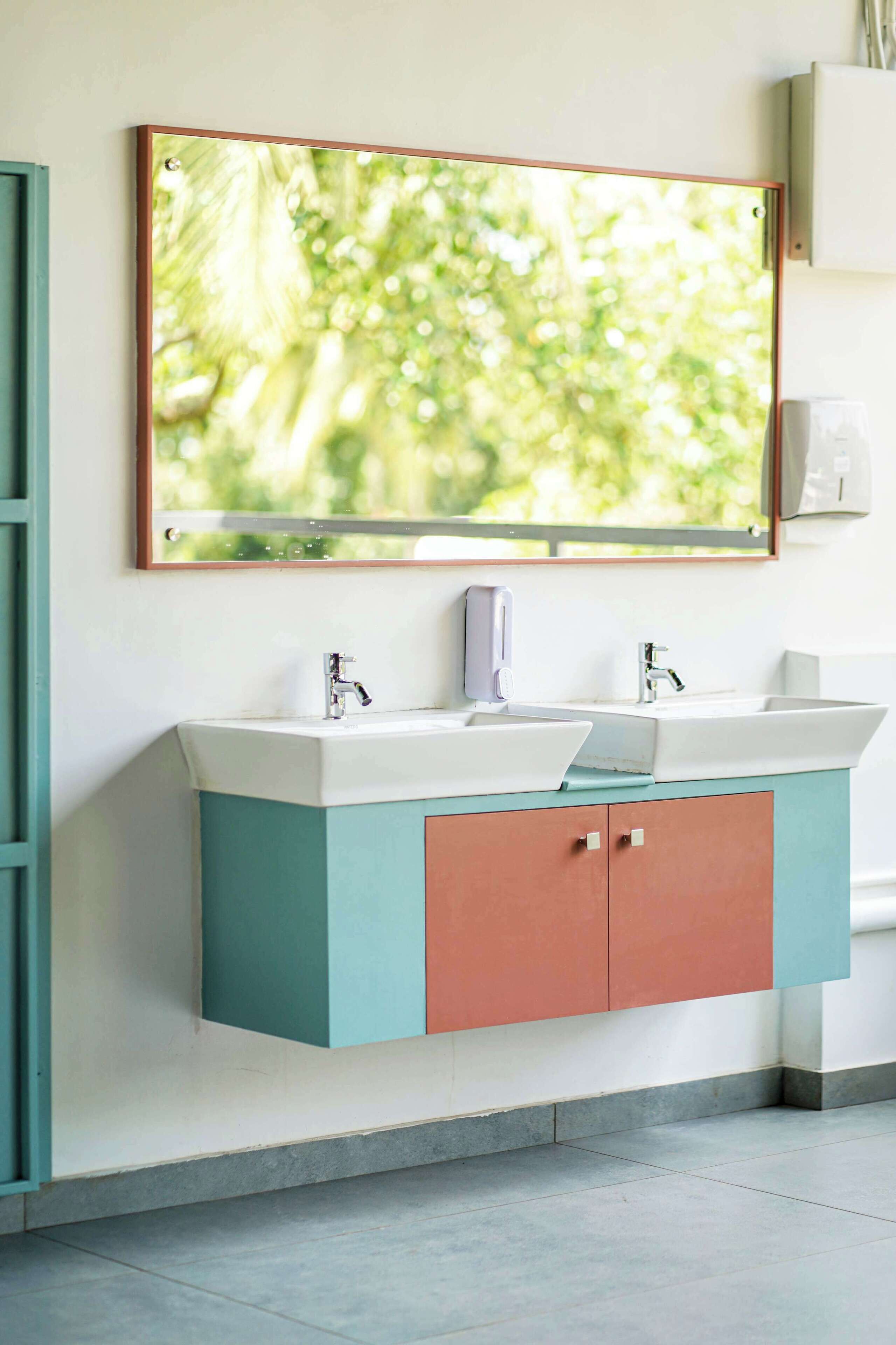 Un baño con lavamanos doble, espejo y ventana con vistas a zonas verdes.