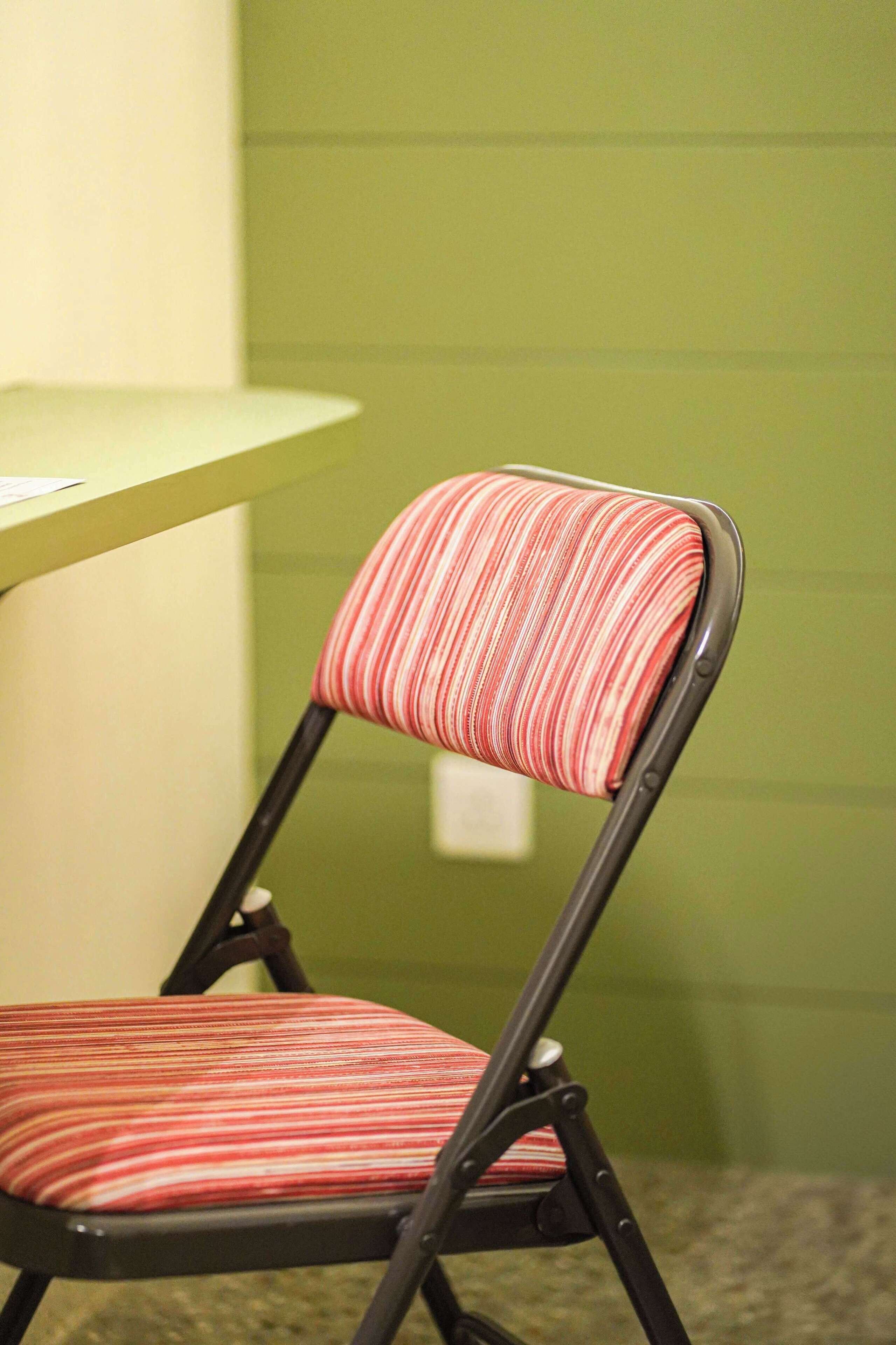 A chair with a striped cushion and a metal frame, positioned against a green wall.