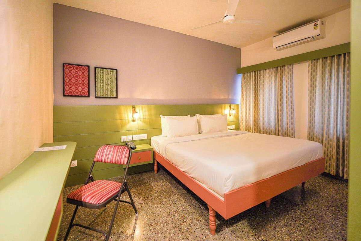 A hotel room with a bed, a desk, a chair, and two wall-mounted lamps.