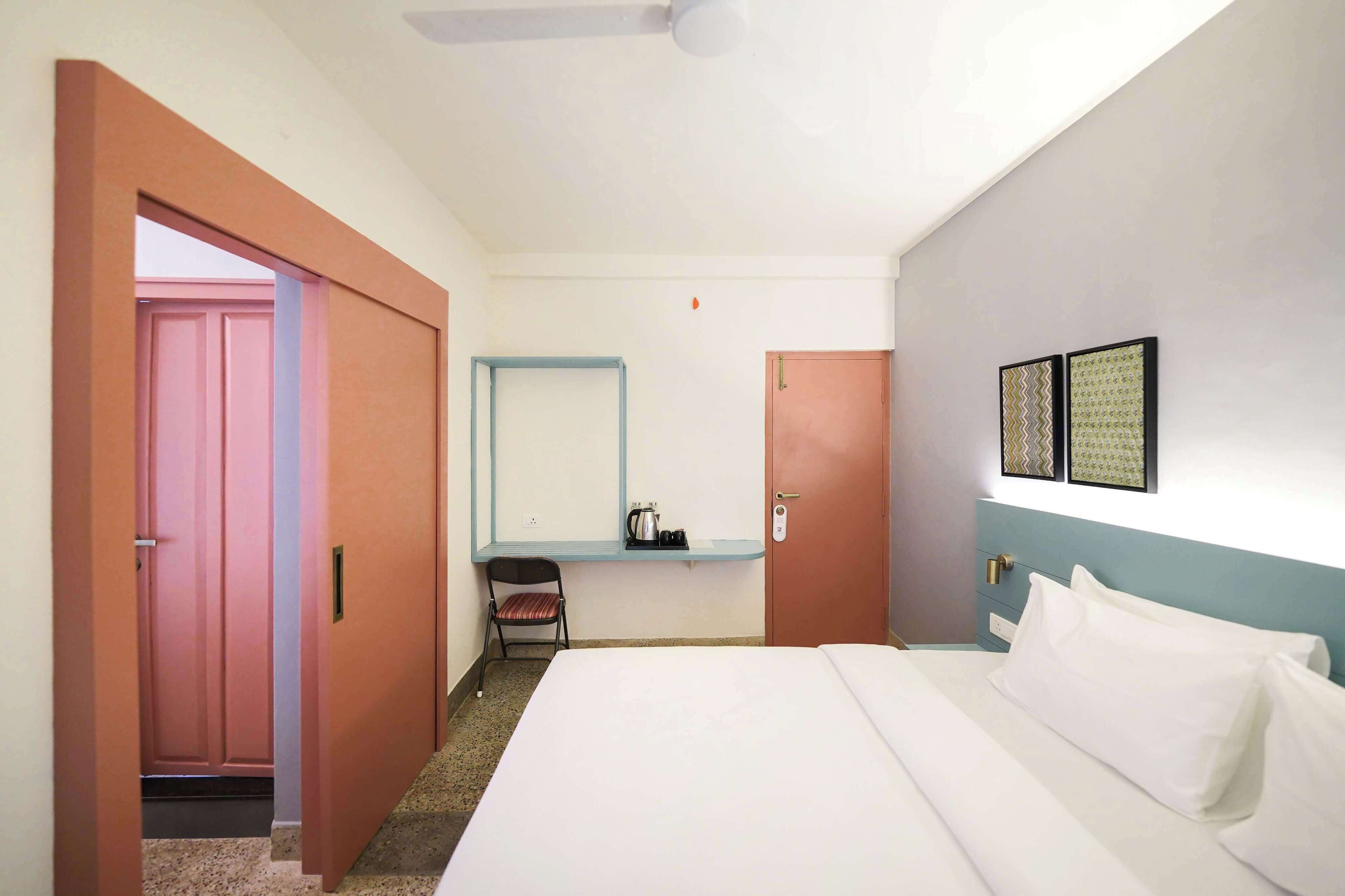 A hotel room with a bed, a chair, a desk with a mirror, and a door.