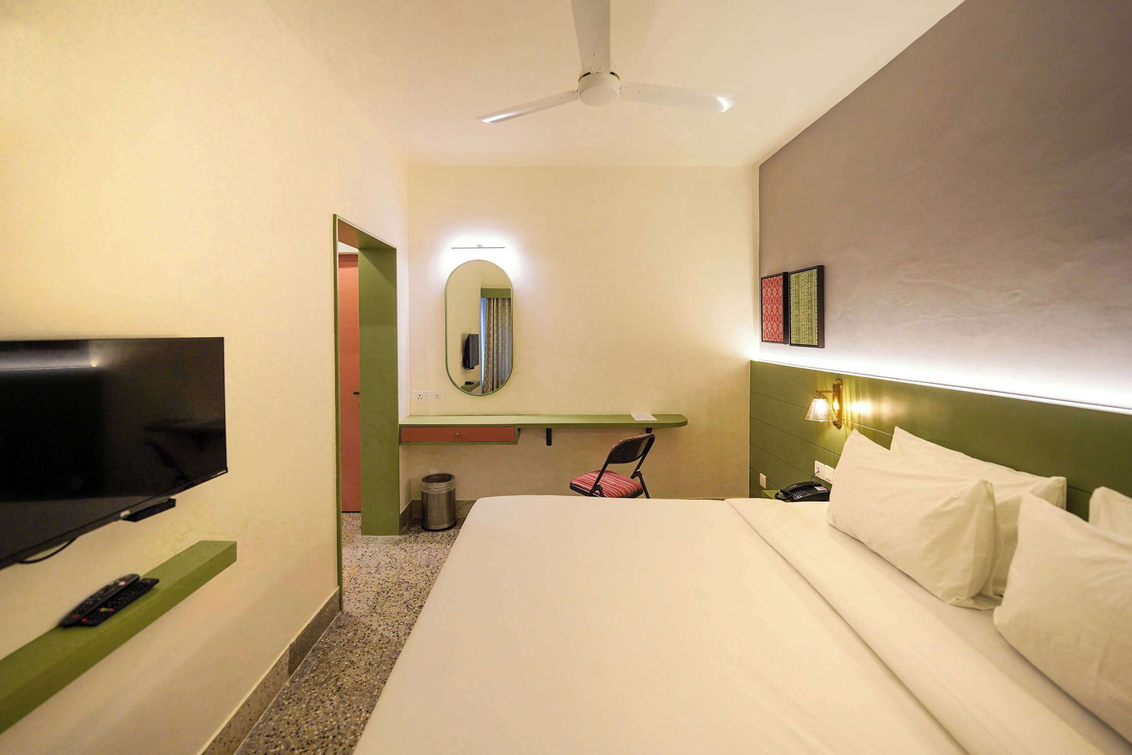 A hotel room with a bed, a television, a mirror, a chair, and a ceiling fan.