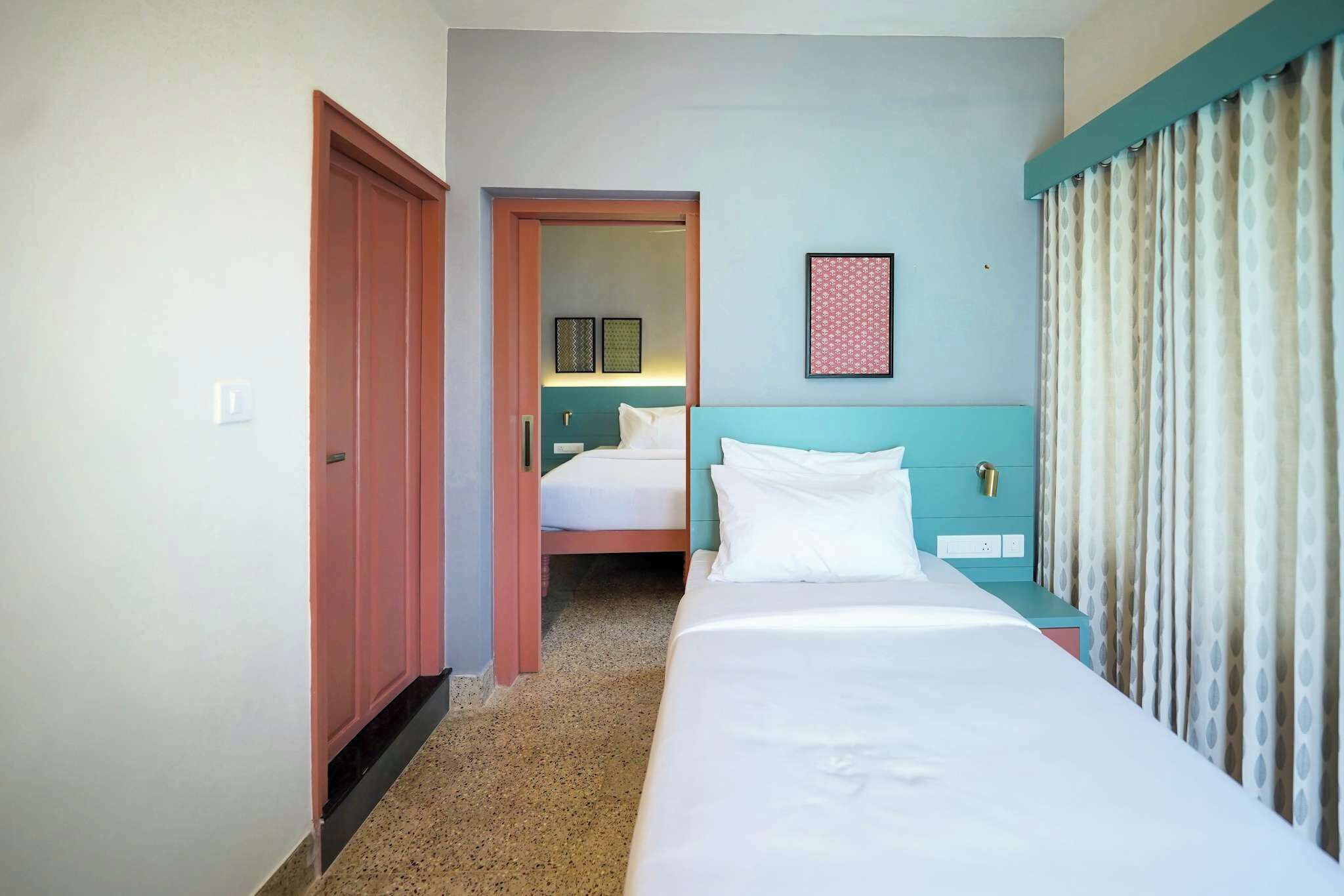 A hotel room with a single bed, a nightstand, a door, and a view of another room.
