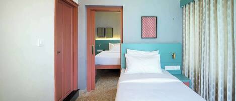A hotel room with a single bed, a nightstand, a door, and a view of another room.