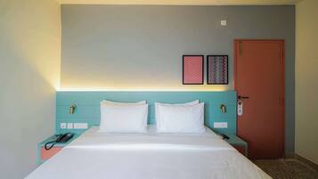A hotel room with a bed, a nightstand with a phone, a door with a lock, and two wall-mounted pictures.
