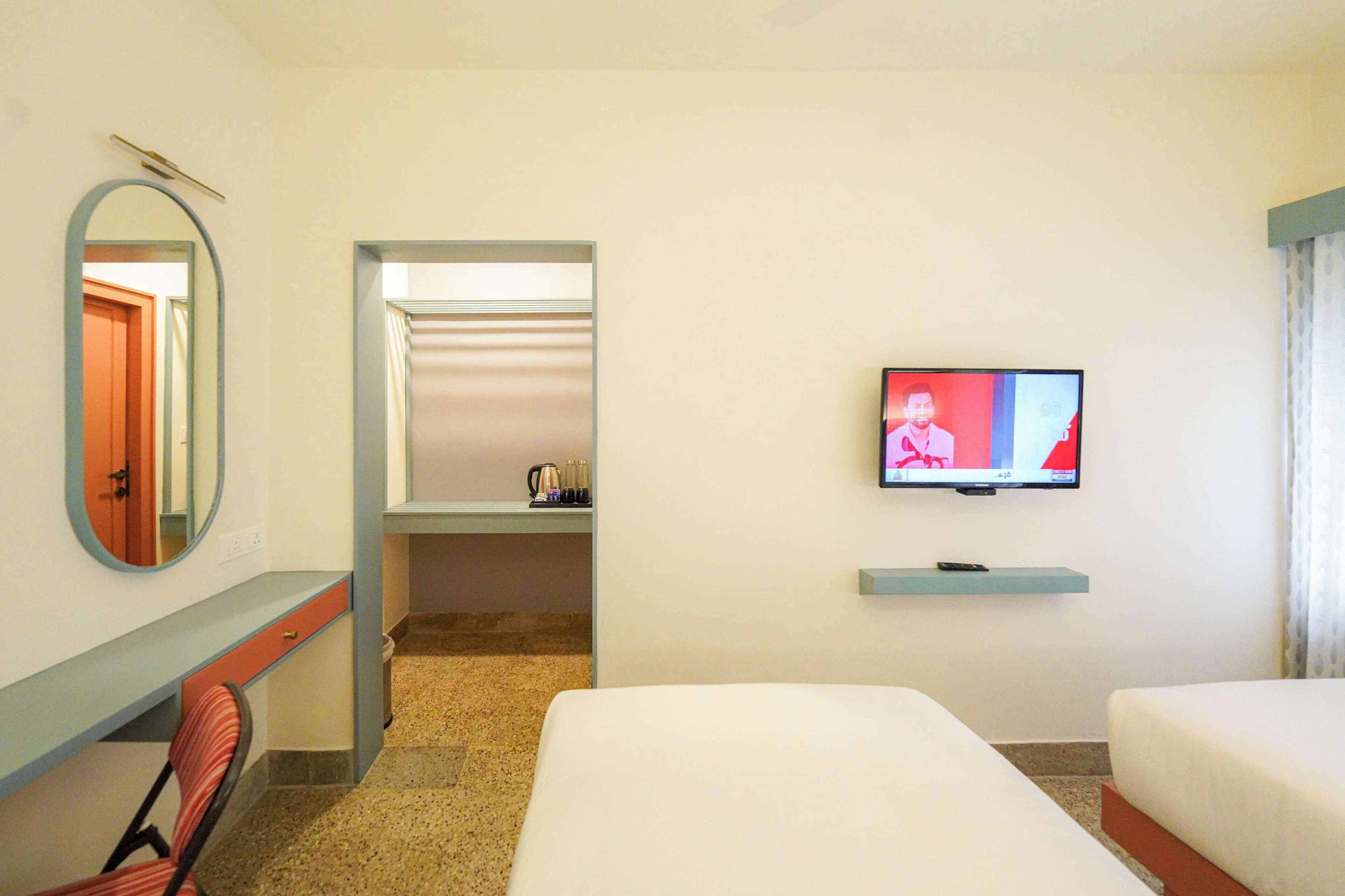 Una habitación de hotel con una cama, un escritorio con una silla, un televisor y un espejo.