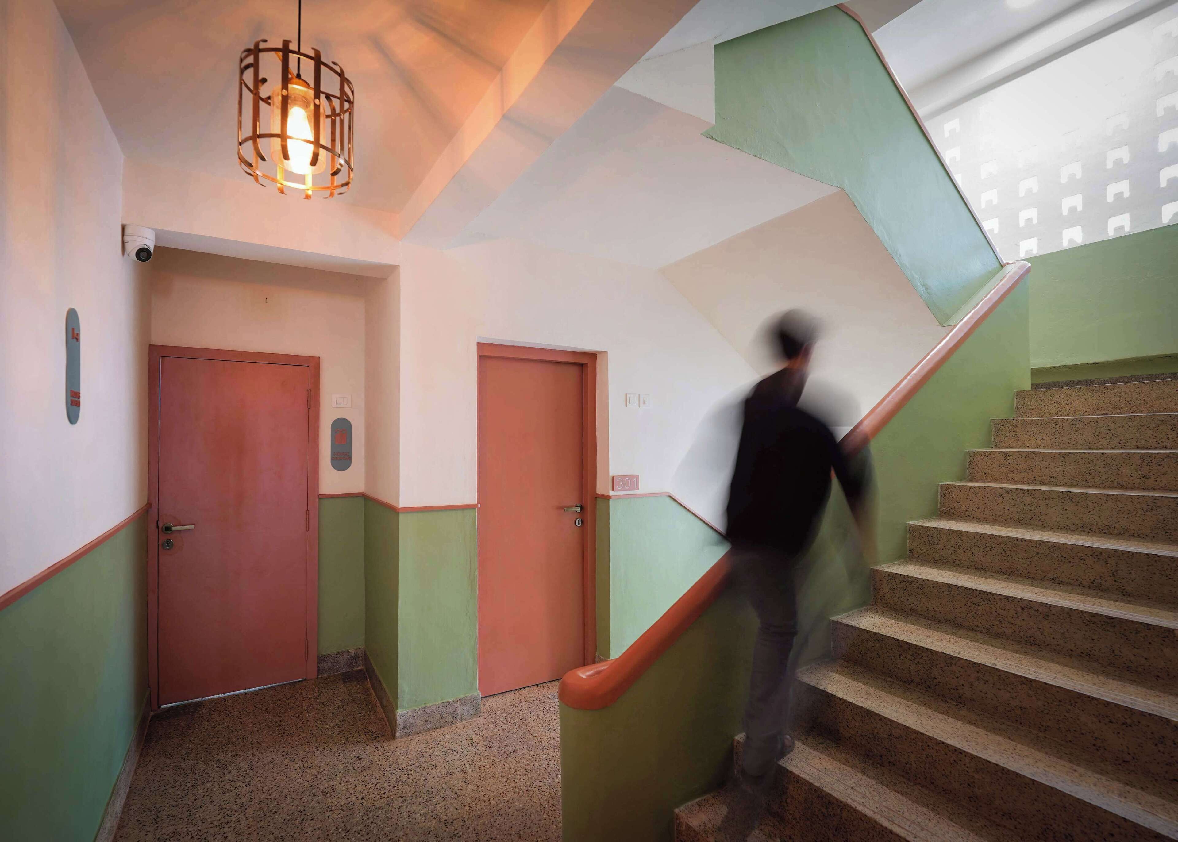 Una escalera con barandilla, una puerta al final e iluminación en el techo.